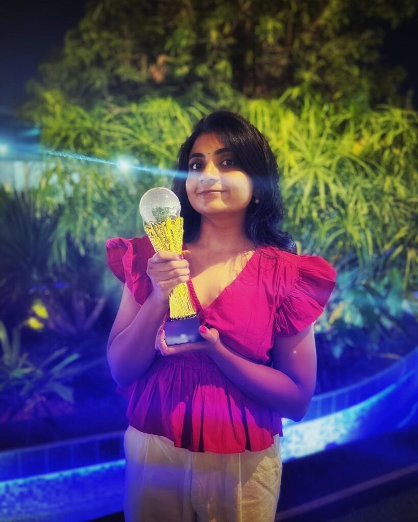 A cheerful and energetic Harika holding an award with a big smile, celebrating success.